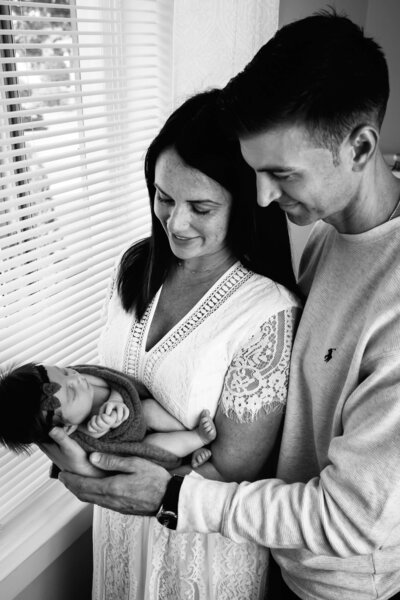 Romantic black and white portrait of new parents kissing above their sleeping newborn baby wrapped in delicate lace fabric