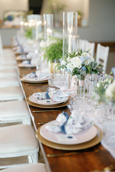 Romantic wedding reception table with subtle pastel florals, glass taper candle holders, and custom napkin wraps at Canyonwood Ridge in Dripping Springs, styled by Eventive Designs.