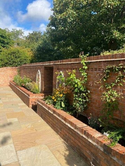 Red brick garden wall with raised flower beds and decorative arched inserts.