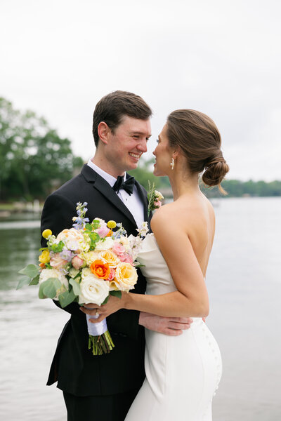 man in black tux holding woman in white dress while she is holding a bouquet of colorful flowers