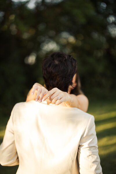 Bride holding hands around the groom's neck. Wedding ring visible in creative shot