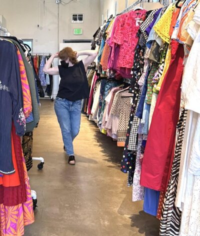 A person dancing as they walk down the aisle of a consignment store 