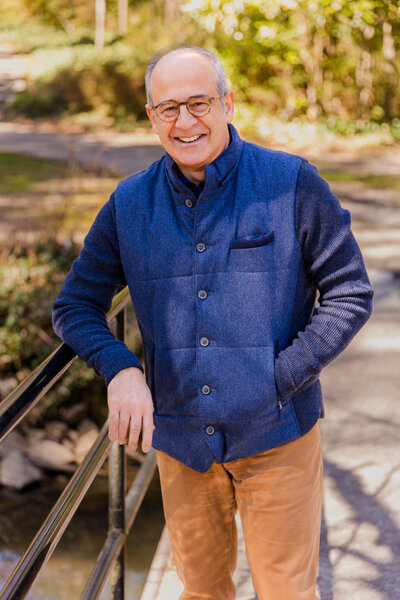 Ahmet Bozer standing on a bridge, hand resting on the handrail, wearing a sleeveless jacket during his outdoor personal brand session in Buckhead Atlanta