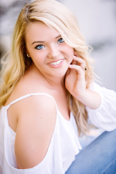 A high school senior girl with long blonde hair, wearing a white blouse smiling at a south shore ma senior photographer