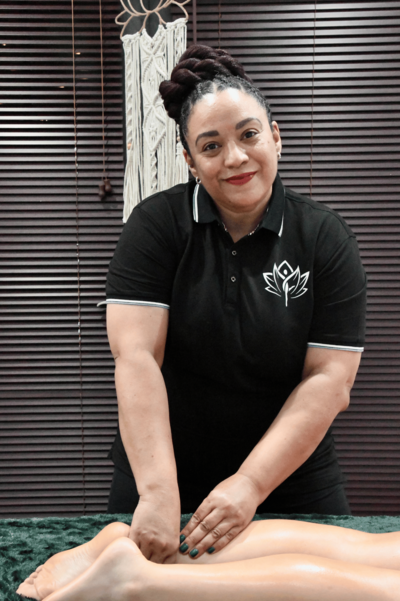 Photo of April Heath smiling wearing a black shirt with the Joyful Rising  Spa logo while massaging a client's calf and ankle
