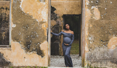A beautiful mother poses in a gray off-the-shoulder dress during her maternity session at Jekyll Island ruins, showcasing her glow. Makeup by Kimberly Mocks enhances her natural beauty.