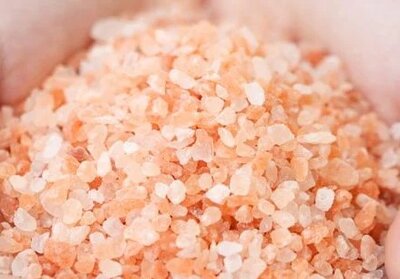 A close-up of two hands gently cupping a pile of pink Himalayan salt crystals, displaying their rough texture and varying shades of pink and white—often used in massage therapy sessions in Tolleson, Arizona.