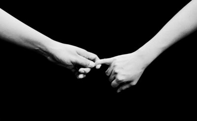 Two hands reaching and one hand holding other hands little finger all on black background