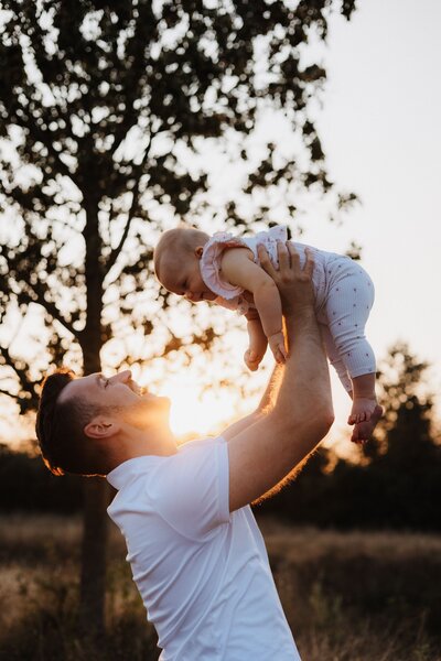 Vater hält Baby während der Golden Hour in die Luft