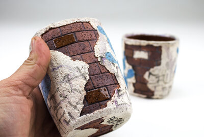 A ceramic cup that resembles plaster falling apart from red bricks with painted cacti and graffiti