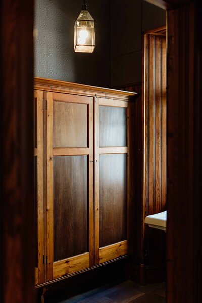 A wooden storage cabinet fills a dark bathroom space. The light is moody and dark.