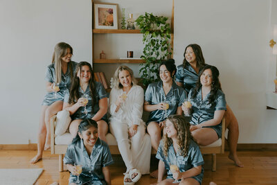 Bride and bridesmaids in matching satin pajamas sharing drinks and laughter while getting ready in the Uliana Estate bridal suite in Lakeland, Florida