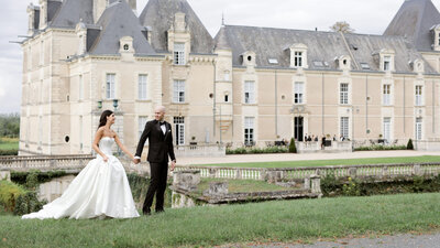 A newlywed couple standing in front of a grand French chateau, surrounded by lush gardens and elegant decor, celebrating their wedding day.