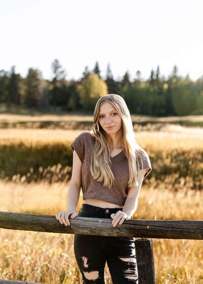 girl smiling in front of fence by a field