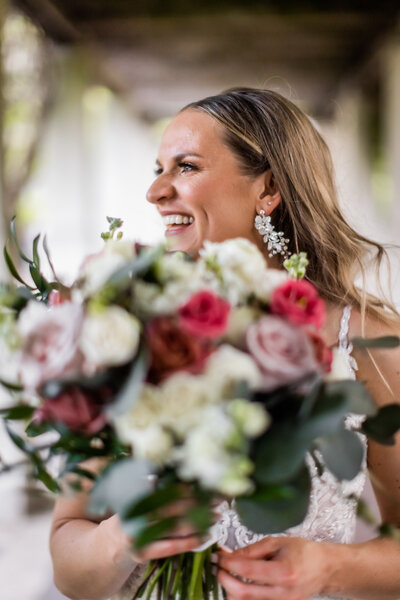 Experience the infectious joy of Sandy's laughter in this charming photo where she holds her stunning bridal bouquet. This image captures a candid, uplifting moment of the bride, her smile radiating as brightly as the beautiful bouquet she cradles. The combination of vibrant flowers and genuine happiness makes this picture a perfect snapshot of a memorable wedding day. Ideal for brides seeking inspiration for their wedding photography, this image showcases how spontaneous laughter and personalized floral arrangements can enhance the beauty of your special day.