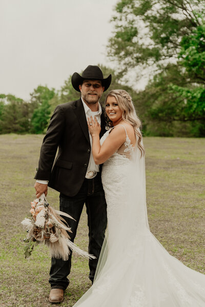 man in black suit holding a bouquet of flowers while woman in white dress hugs him 