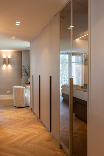 Slaapkamerinterieur met een ingebouwde kastopstelling met spiegels en houten afwerking, onderdeel van een compleet interieurproject.
