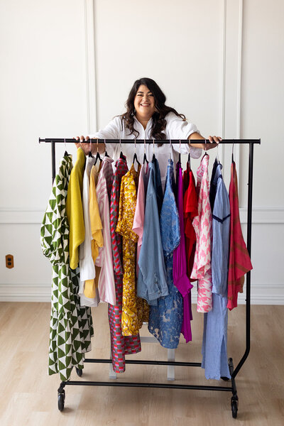 Marissa Martinez standing behind a rack of colorful clothes on hangers
