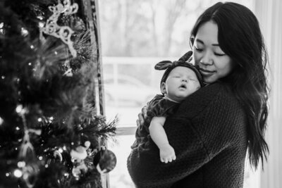 Smiling mom looking at newborn daughter in her relaxed home with candid pose, family photo session in North east Ohio