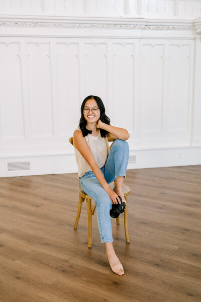 woman sitting on a chair holding a camera smiling