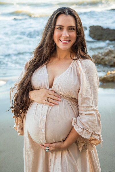 Woman holding pregnant belly with Pacific Ocean in background | California Maternity Session