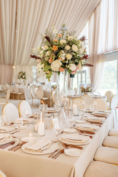 Wedding reception table with neutral tones, tall floral centerpiece, and candles.