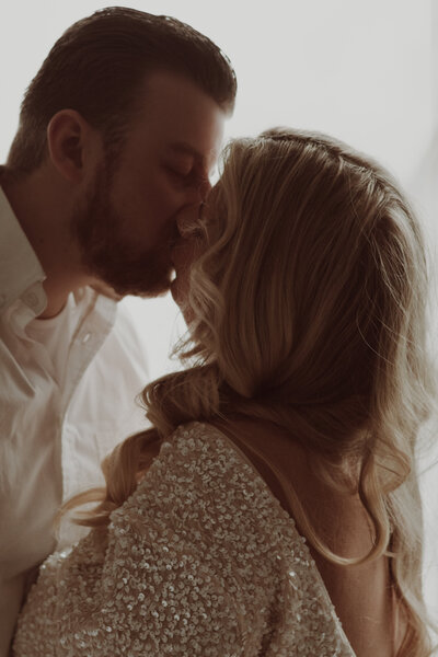 Een man en vrouw kussen voor een raam, omringd door een warme, romantische sfeer.