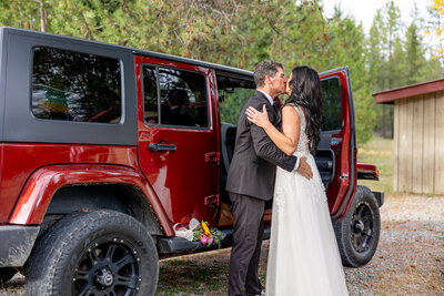 Bride and groom hugging while getting in a red Jeep Wrangler
