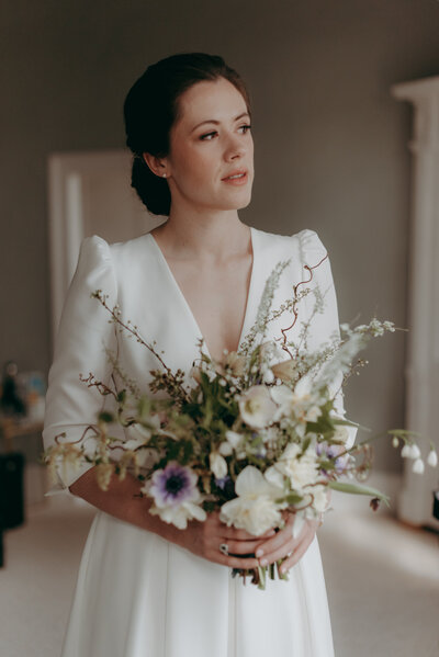 Bride standing by a window holding a bouquet