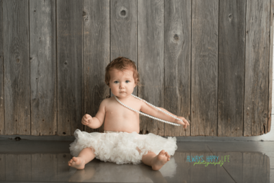Baby girl sits for one year old picture holding pearls in a  photography studio near South Bend.