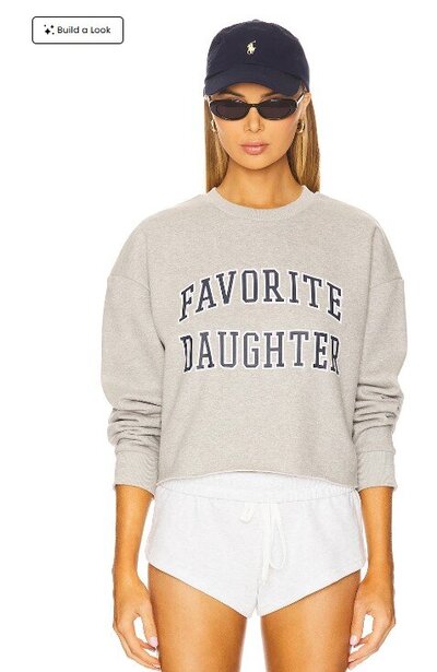 Model wearing a grey Favorite Daughter sweatshirt, white drawstring shorts, black sunglasses, and a navy Polo cap — a sporty fall tailgating look.