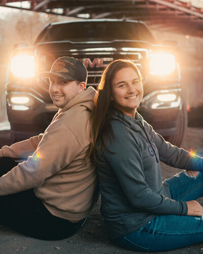 A couple sits back to back in front of their new truck under the twin bridges during their couples session near Albany, NY.