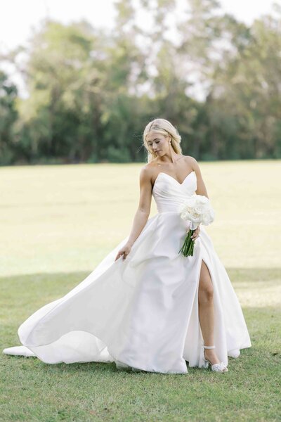 a bride posing for a portrait while holding the side of her wedding dress train