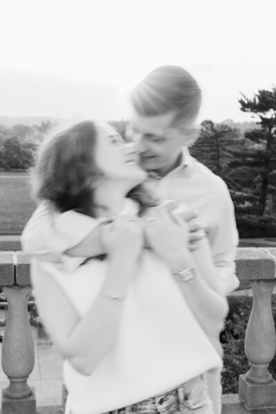 A young woman leans back to kiss her fiance at the top of Ault Park as the sun sets behind them
