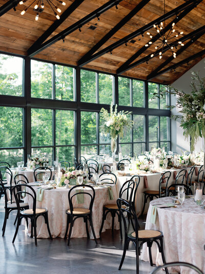 view of a reception table with a tall floral arrangement in the middle and big windows, designed by wedding planners in Columbus Ohio, Sirpilla Soirees