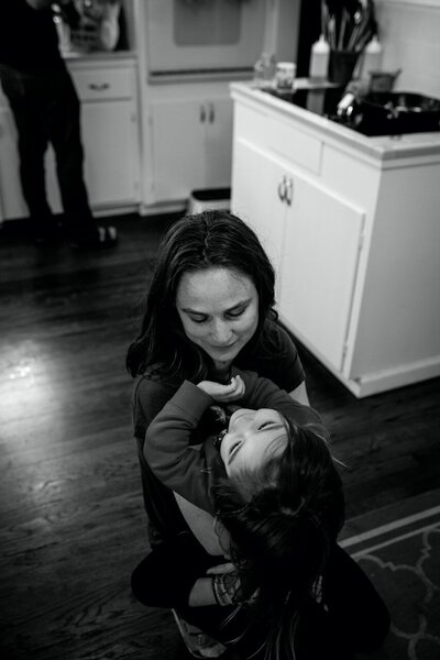 Mom holds her daughter on the floor of their kitchen while she giggles. 