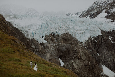 Couple walks to an overlook with a giant glacier towering in the distance