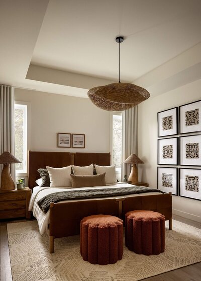 Serene Japandi primary bedroom featuring a leather king bed, organic rattan pendant light, abstract tribal-inspired artwork, boucle ottomans, and soft, textured bedding.