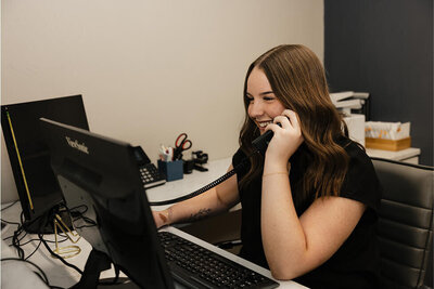 The secretary running the front desk is on the phone smiling as she speaks to a patient on the phone.