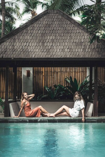 two blonde girls one wearing peach dress and one wearing white dress sitting by pool at a villa in gili trawangan