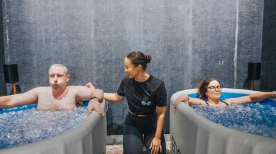A participant in an ice bath breathes deeply, supported by a breathwork coach, in a serene and focused cold immersion session.