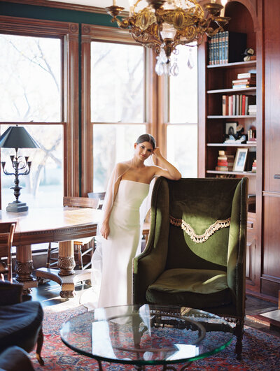 Bride in an elegant room leaning against a green chair