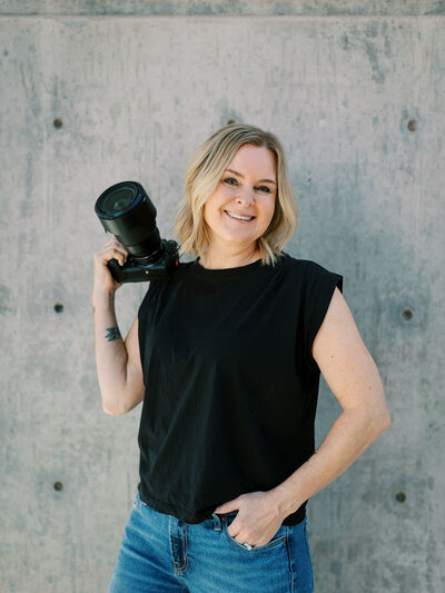 A photographer smiling while holding a camera up to her shoulder.