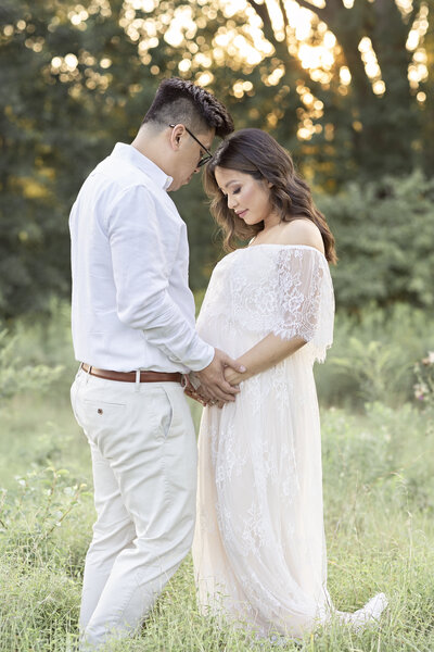 pregnant couple facing each other looking at pregnant belly in green field maternity pictures