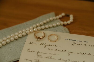 Wedding rings, pearl necklace, and handwritten letter on a table.