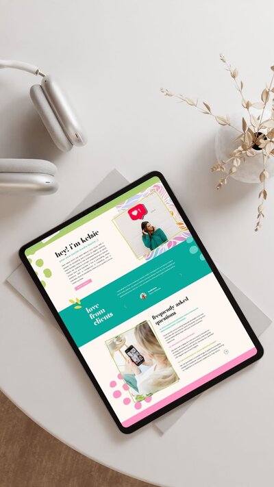 A tablet displaying a colorful showit website template is placed on a round table next to headphones and a small vase with dried flowers, ready for the VIP launch day celebration.