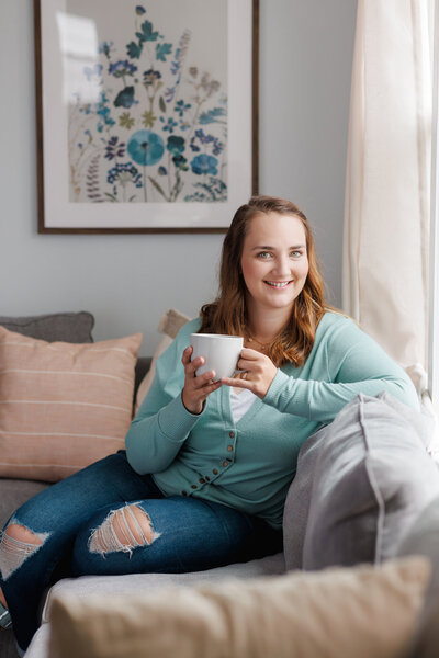 Emily drinking a cup of coffee, smiling, sitting on the couch