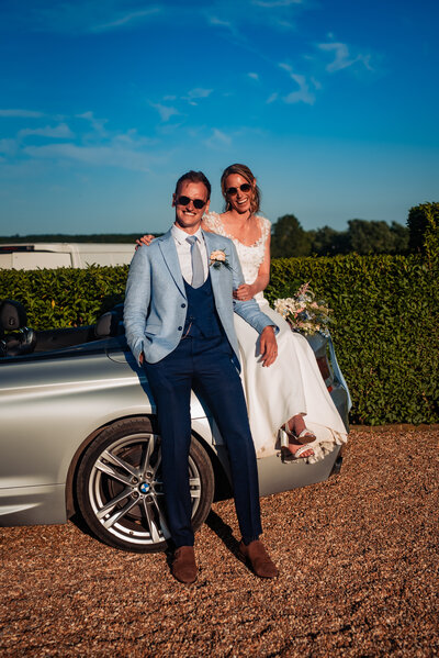 couple being playful, bride is wearing a white suit and groom is wearing a navy suit, embracing each other.
