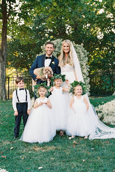 Joyful wedding family portrait featuring the bride, groom, flower girls, ring bearer, and their dog — elegant outdoor celebration captured by Asia Pimentel Photography.