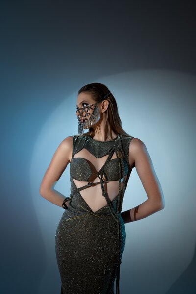 Model posing in a revealing dress with a metallic mask covering half her face, showcasing edgy and bold fashion